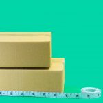 Cardboard boxes with tape measure on green background.