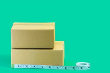 Cardboard boxes with tape measure on green background.