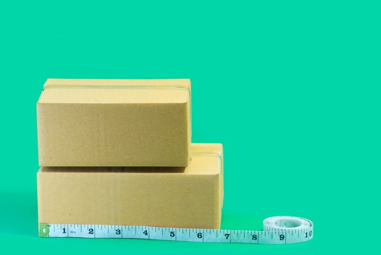 Cardboard boxes with tape measure on green background.